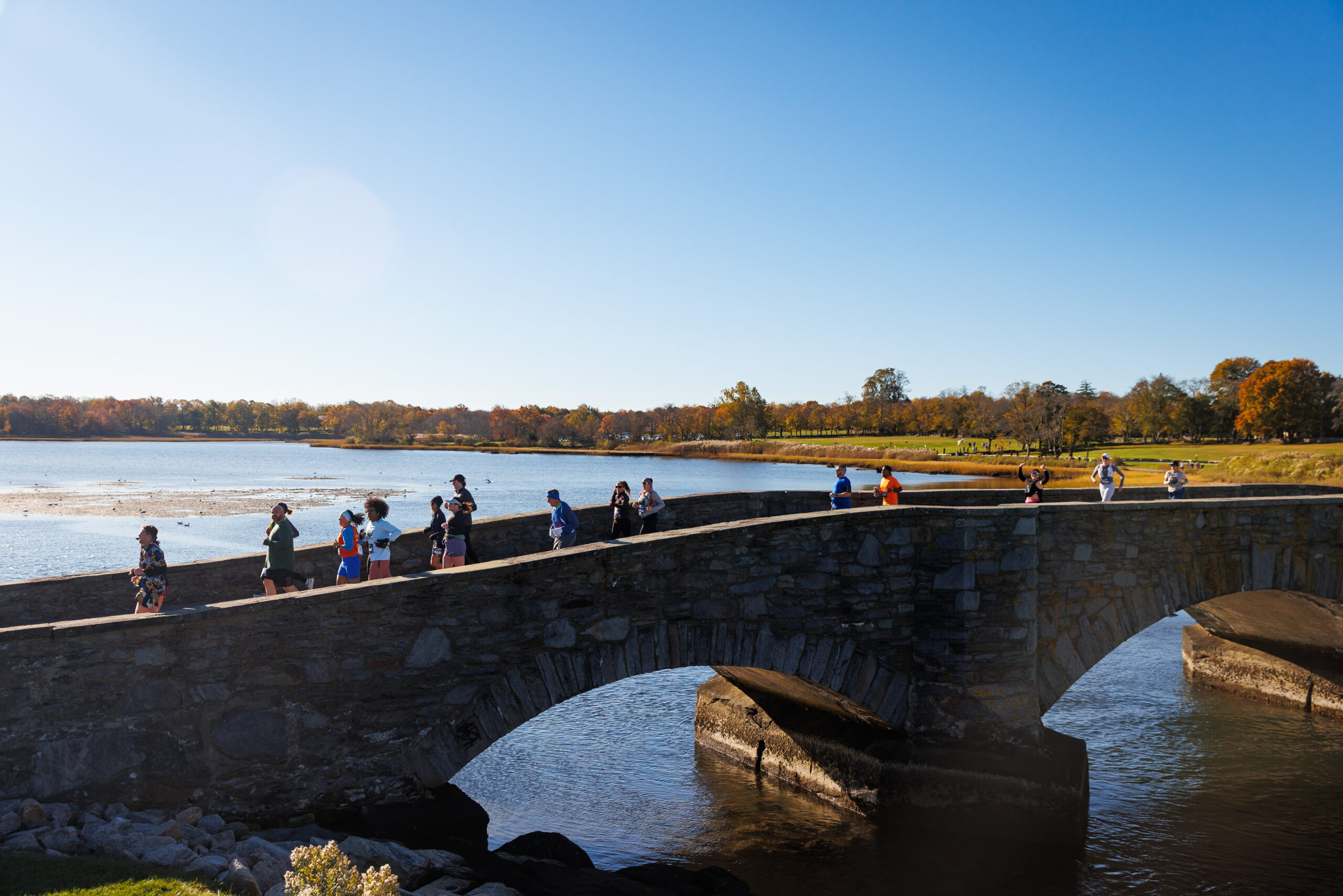 Runners crossing the stone bridge at Colt State Park Half Marathon.